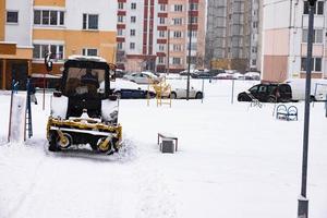 The tractor clears the road from snow in winter during a snowfall. photo