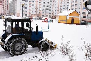 The tractor clears the road from snow in winter during a snowfall. photo