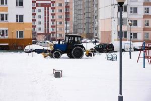 The tractor clears the road from snow in winter during a snowfall. photo