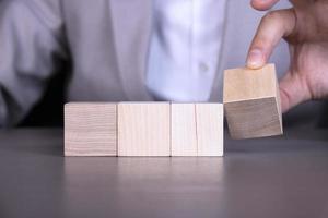 A businessman adds four wooden cubes with empty space for icons, free space for letters, numbers, symbols or labels. photo