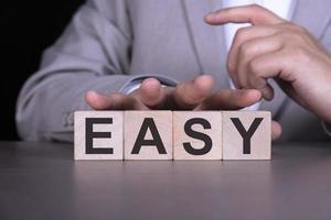 EASY, the word is written on wooden cubes, blocks on the background of a man, a businessman in a gray suit. photo