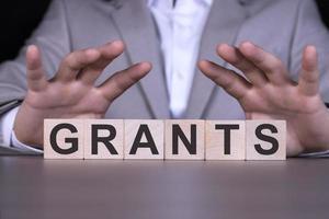 GRANTS, the word is written on wooden cubes, blocks on the background of a man, a businessman in a gray suit. photo