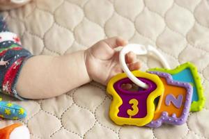 Hand of a baby lying on a bed with a toy symbol, three months from birth. Close-up of a palm. Fatherhood and children day concept. photo