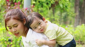 A boy happily rides on his mother's back in the park during the holidays. concept of love between mother and son video