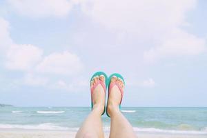 Young people wear the shoes sandals closeup show feet relaxing on beach on sand enjoying chill sun on sunny summer day. Enjoying the sea photo