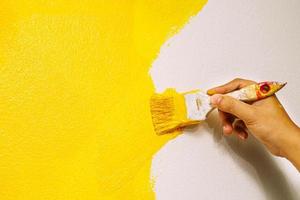 Paint brush, close up hand painter worker painting on surface wall Painting apartment, renovating with yellow color paint. Leave empty copy space to write descriptive text beside. photo