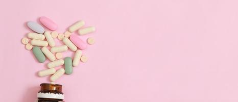 Pill bottle spilling out. colorful pills on to surface tablets on a table pink background. top view. drug medical healthcare concept photo