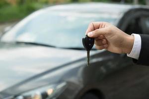 la llave del auto, el hombre de negocios entrega la llave del auto al otro hombre en el fondo del auto. foto