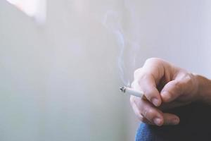 hombre sosteniendo fumando un cigarrillo en la mano. propagación del humo del cigarrillo. fondo oscuro foto
