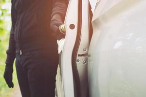 Close up hand pulling the handle of a car thief  wearing black clothes and glove stealing automobile trying door handle to see if vehicle is unlocked  trying to break into. car theft concept. photo