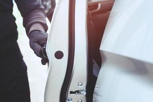 Close up hand pulling the handle of a car thief  wearing black clothes and glove stealing automobile trying door handle to see if vehicle is unlocked  trying to break into. car theft concept. photo