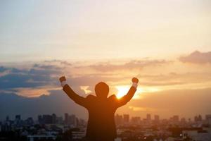 silhouette hand raised fist business man with sun lighting in morning. background city, success, grow up. photo