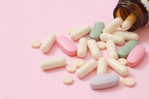 Pill bottle spilling out. colorful pills capsule on to surface tablets on pink background. drug medical healthcare pharmacy concept. pharmaceuticals antibiotics pills medicine in blister packs. photo