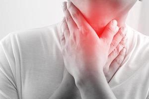 sore throat pain. Closeup of young man sick holding her inflamed throat using hands to touch the ill neck in blue shirt on gray background. Medical and healthcare concept. Focus red on to show pain. photo