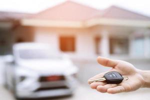 Business man hand holding car keys front with new car on background. parking in front of the house. transportation concept. Leave copy space to write messages text. photo