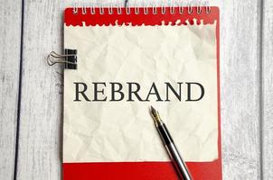 rebrand, text on white paper and red notepad on wooden background photo