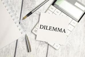 Text DILEMMA on paper card and calculator on wooden background photo