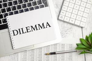 Notepad with the text DILEMMA on laptop capacity photo