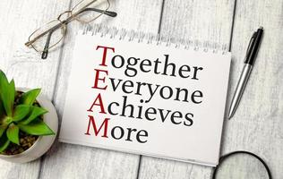 together everyone achieves more words and calculator, pen and glasses on wooden background photo
