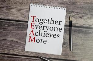 together everyone achieves more words on wooden background and pen photo