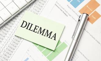 Text DILEMMA on paper card and calculator on wooden background photo