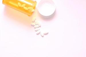 Oval pills and orange pill bottles were spread out on the white tabletop. photo