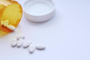 Oval pills and orange pill bottles were spread out on the white tabletop. photo