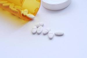 Oval pills and orange pill bottles were spread out on the white tabletop. photo