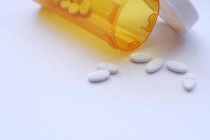 Oval pills and orange pill bottles were spread out on the white tabletop. photo