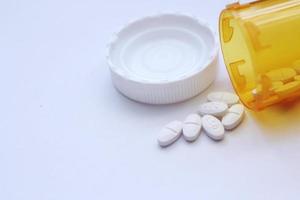 Oval pills and orange pill bottles were spread out on the white tabletop. photo