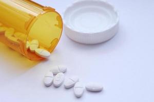 Oval pills and orange pill bottles were spread out on the white tabletop. photo