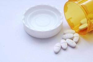 Oval pills and orange pill bottles were spread out on the white tabletop. photo