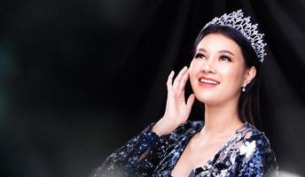 Portrait of Miss Pageant Beauty Contest in blue sequin Evening Ball Gown with sparkle light Diamond Crown, Asian Woman feels happy smile and poses many difference style over dark smoke photo