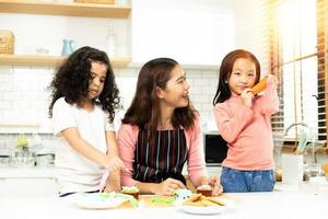 grupo de familia diversa, niño árabe africano asiático y árabe en edad preescolar hacen pasteles en la cocina, la madre prepara una decoración bonita con diversión educada en la merienda. desorden de crema en toda la cara, espacio de copia foto