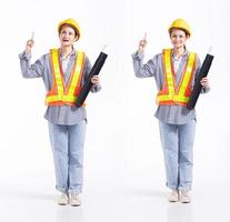 Mujer contratista de ingenieros de carrera mixta de longitud completa de 20 años, señalando con el dedo en el aire vacío, use guantes de seguridad para cascos grandes. Los soportes femeninos de la oficina sienten una sonrisa feliz sobre un fondo blanco aislado foto