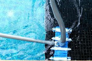 Worker clean private swimming pool with vacuum blue tube cleaner every week in Summer photo