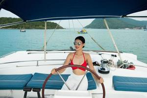 Beautiful Asian mix race Tanned skin Woman walk along Luxury Yachts in deep ocean, Red bikini sunglasses Girl posing as Fashion Model in docking pier under summer blue sky in vacation holiday photo