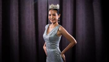 Miss Pageant Beauty Contest wears sequin Evening Gown long dress with sparkle Diamond Crown, Asian Woman opens purple Curtain after win Final round as new way life, opportunity, change, isolated photo