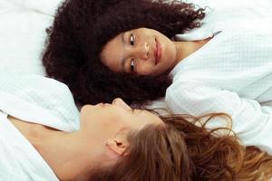 Caucasian and black women love together and lying on bed as diversity person. Young Adult Romantic couple look at each other face and express feeing happy smile and diversity freedom, copy space photo