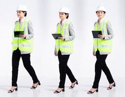 Full length 20s young Mix Race engineer architect client Woman, walking forward left right, wear safety vast hardhat tablet. Office female stands feels smile happy over white background isolated photo