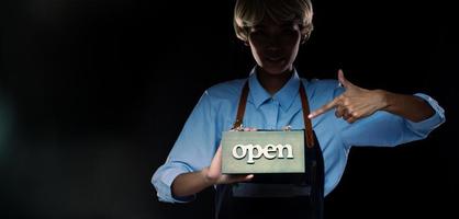 Caucasian person hold Open Sign Business to show service at door entrance store, cafe, retail and welcome shop. Happy Entrepreneur female blonde hair wear waitress dress as open business time concept photo