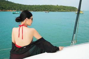 Beautiful Asian mix race Tanned skin Woman walk along Luxury Yachts in deep ocean, Red bikini sunglasses Girl posing as Fashion Model in docking pier under summer blue sky in vacation holiday photo