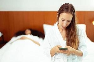 Caucasian and black women love together and lying on bed as diversity person. Young Adult Romantic couple check smart phone behind her back for secret chat text as jealous feeling, copy space photo