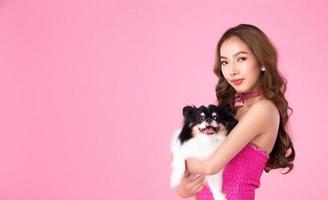 Girl wear chocky Pink dress hold cute dog and look at camera over pink background photo