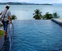 Woman Worker clean private swimming pool with vacuum blue tube cleaner every week in Summer, Salt type Pool along with Ocean as horizontal style with coconut trees