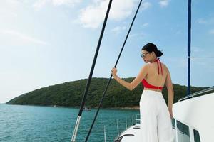 Beautiful Asian mix race Tanned skin Woman walk along Luxury Yachts in deep ocean, Red bikini sunglasses Girl posing as Fashion Model in docking pier under summer blue sky in vacation holiday photo