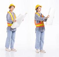 Mujer contratista de ingeniería caucásica de longitud completa de 20 años, que parece trabajar duro, usa un gran plano de casco de seguridad. Los soportes femeninos de la oficina sienten una sonrisa feliz sobre un fondo blanco aislado foto