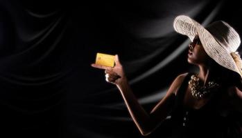 silueta de mujer joven con tarjeta de crédito dorada comprar vender en línea sobre fondo negro de cortina foto