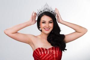 retrato del concurso miss pageant en vestido de noche de lentejuelas rojas asiáticas con banda de corona de diamantes plateados, peinado de cara de maquillaje de moda, iluminación de estudio fondo blanco espacio de copia aislado foto