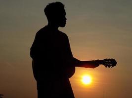 silhouette of a person playing guitar on a sunset background photo